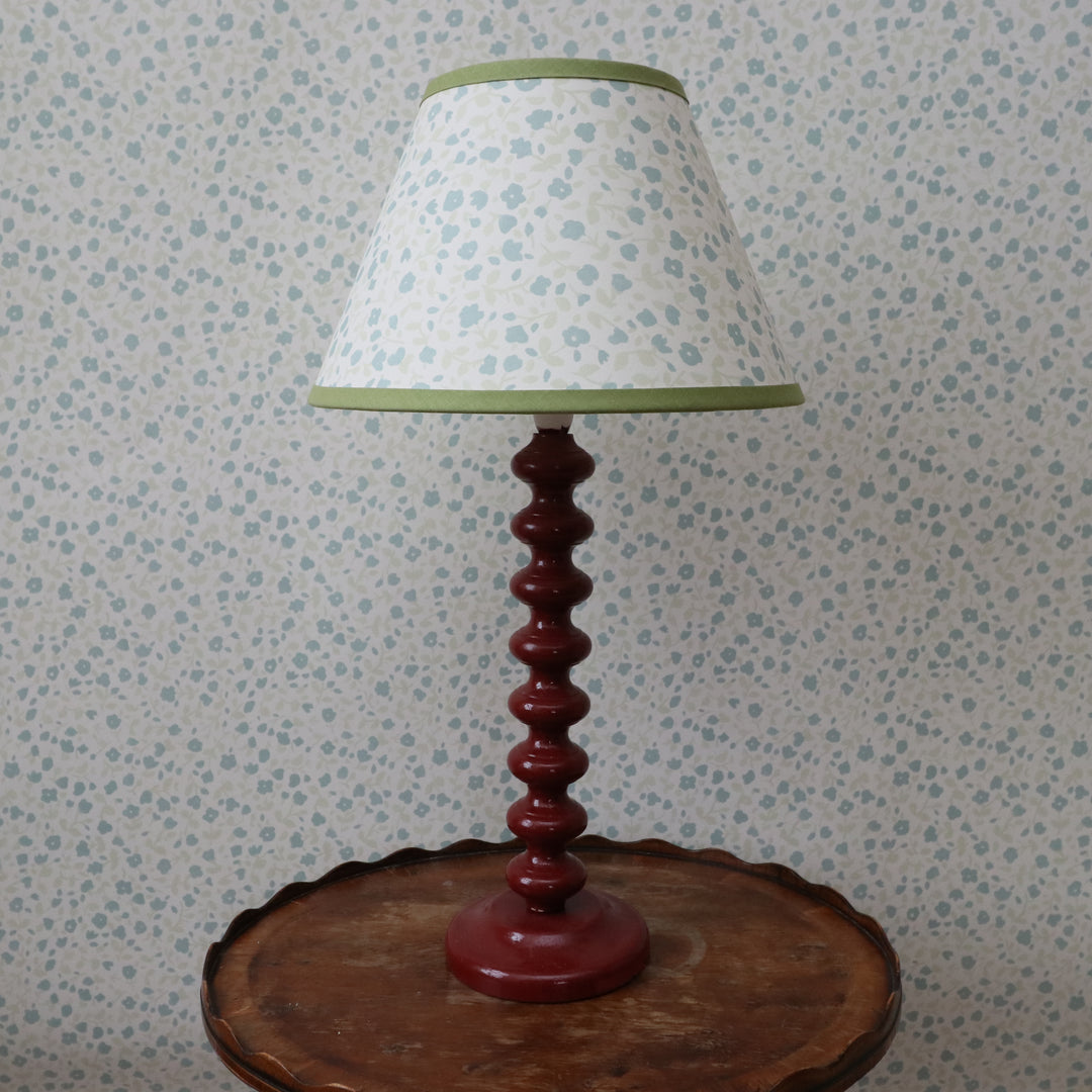 Lamp with a patterned shade on a wooden base against a floral wallpaper background